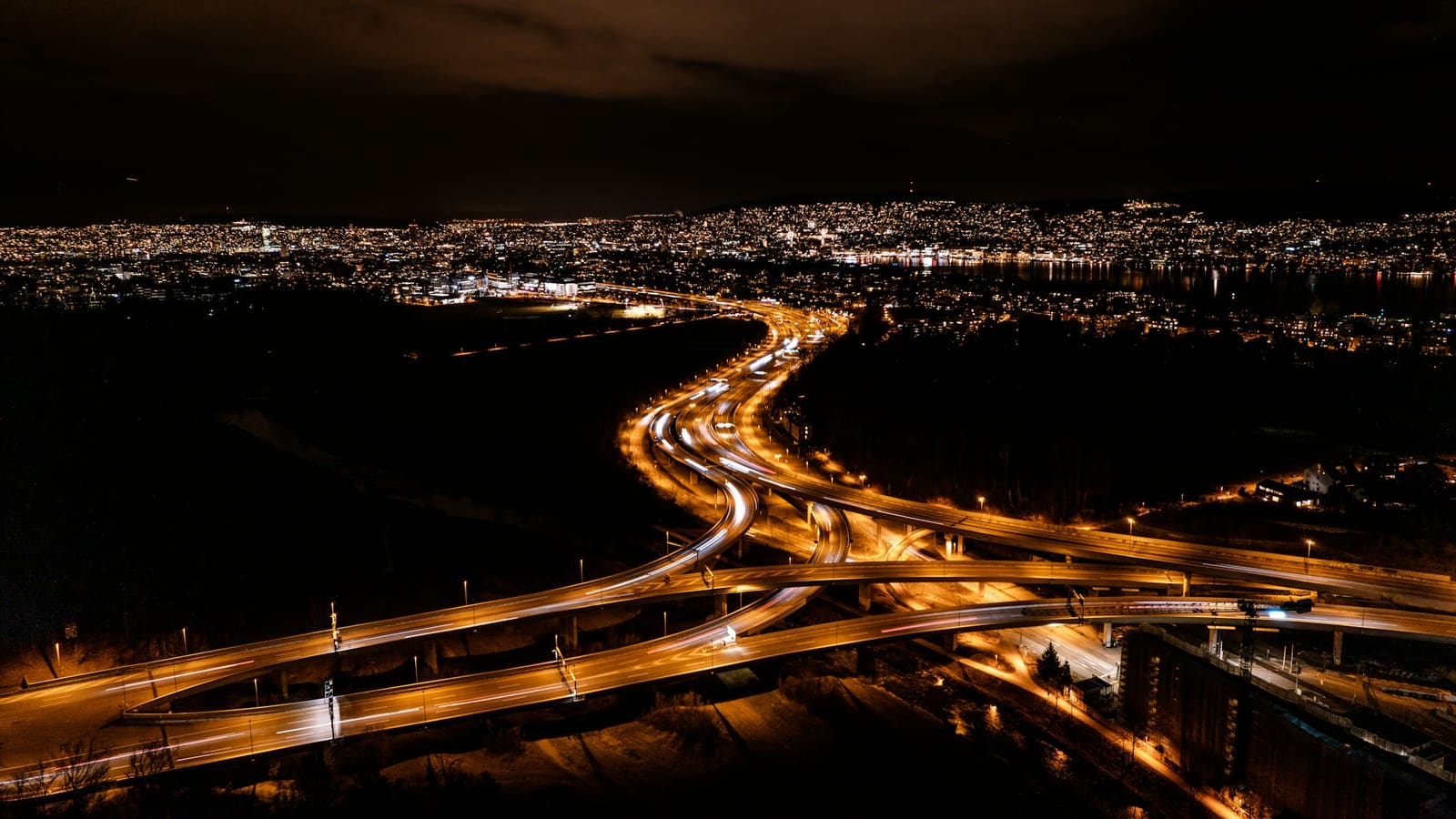 Aerial view of a glowing highway interchange winding toward a city lit at night