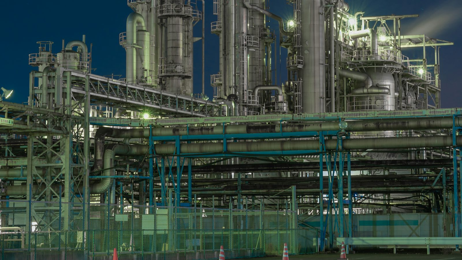 A process plant at night, with distillation columns, pipe racks and steel walkways lit in green